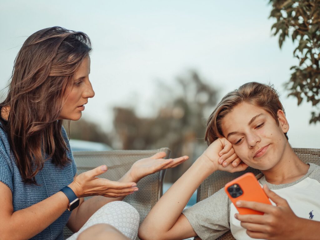 "Mother talking to her teenage son while he uses his smartphone at home, showing parent-teen communication during adolescence."